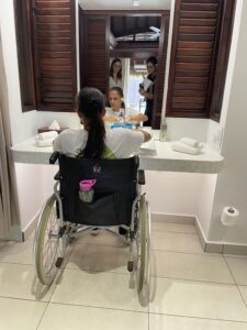 Test en fauteuil pour l'accessibilité de la salle de bain du bungalow PMR. La chargée de communication en fauteuil devant le lavabo et le miroir pour tester la hauteur